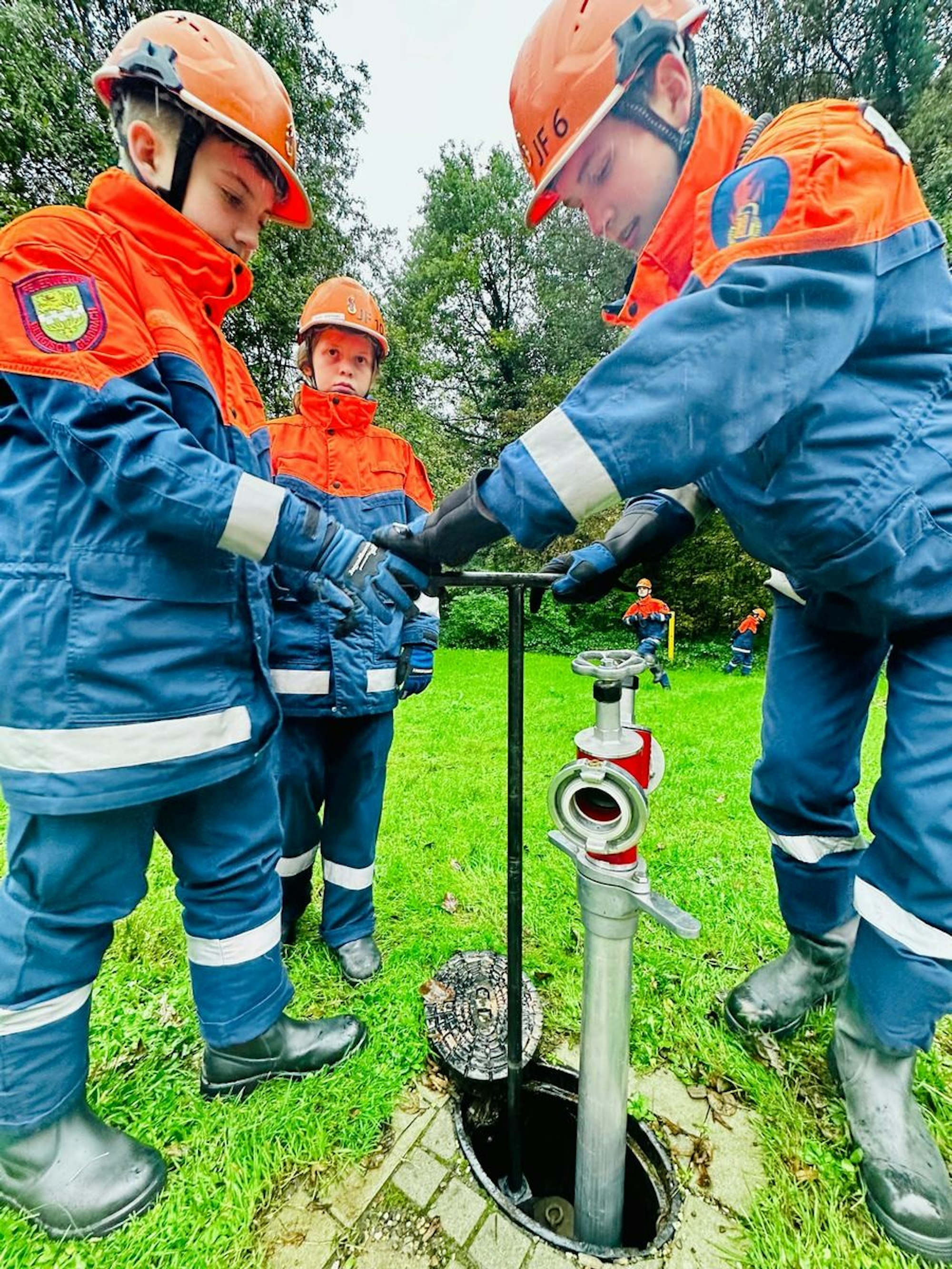 Drei Jugendfeuerwehrleute schließen einen Hydranten für Löschwasser an.