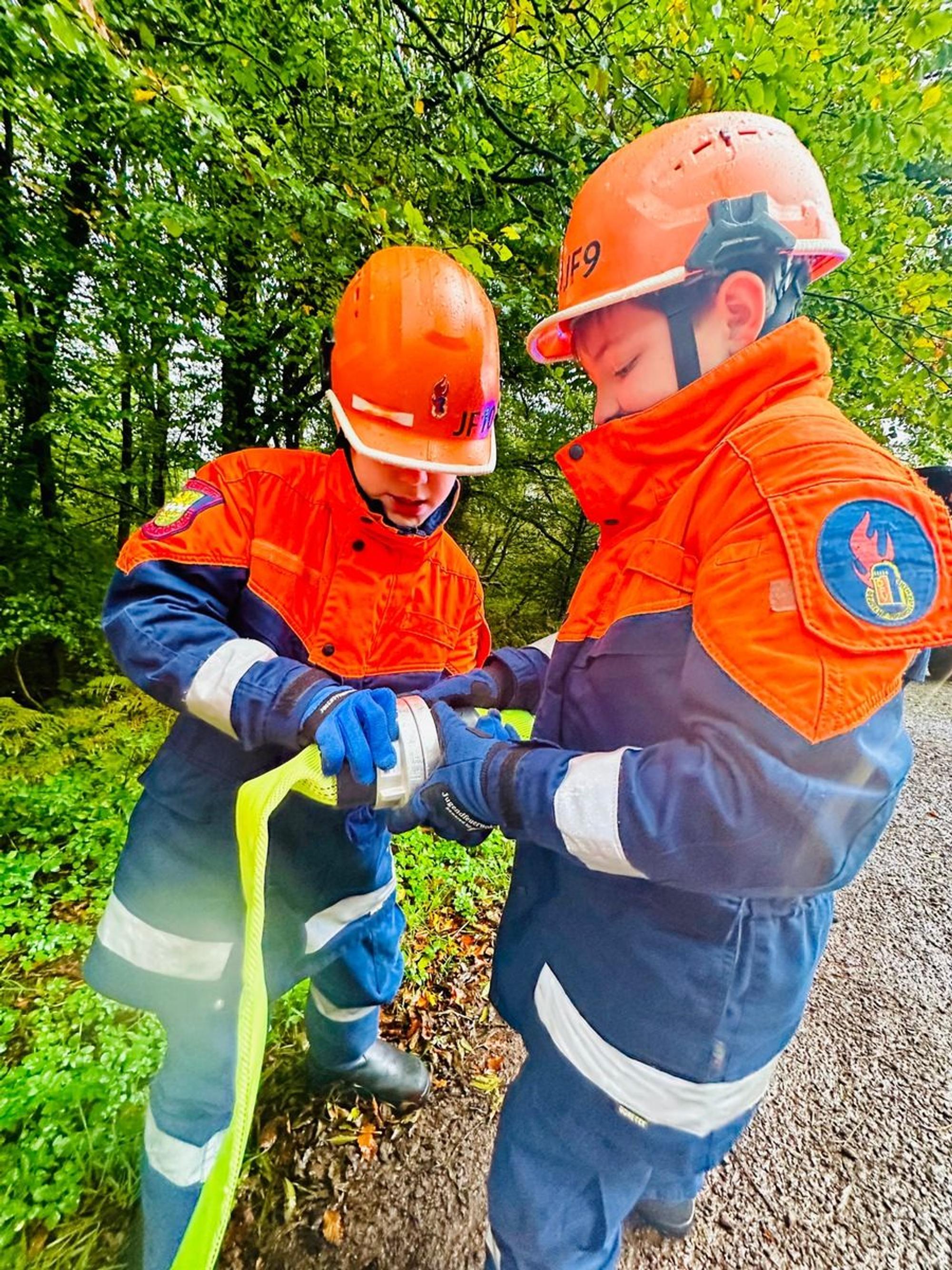 Zwei Jugendfeuerwehrleute koppeln Schlauchstücke aneinander.