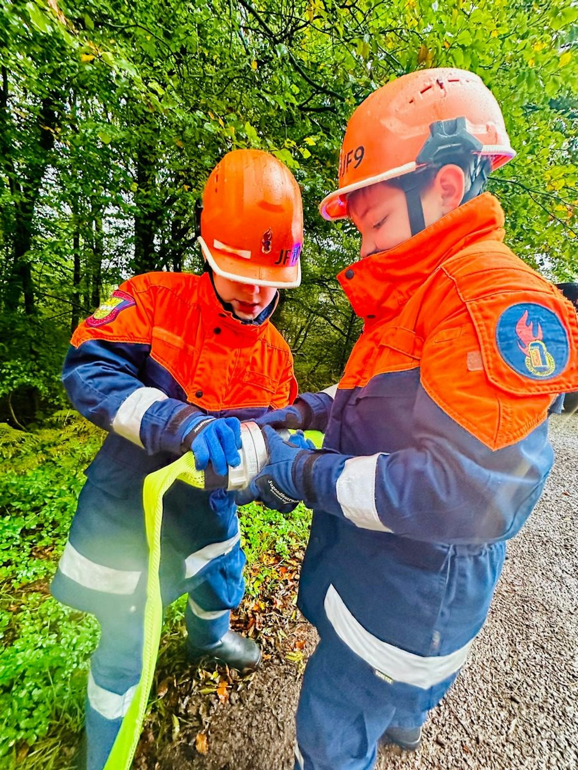 Zwei Jugendfeuerwehrleute koppeln Schlauchstücke aneinander.