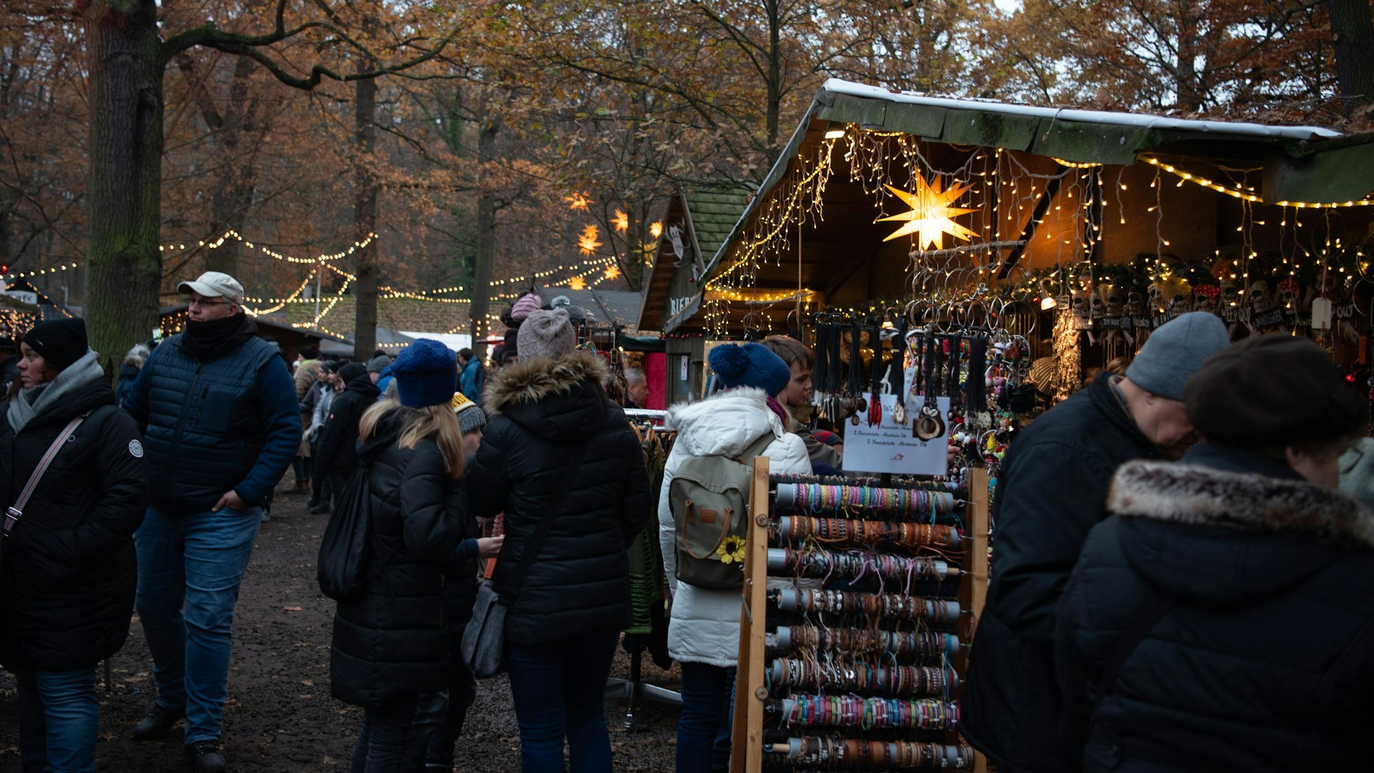 Zahlreiche Besucher gehen an mit Lichterketten geschmückten Buden vorbei.