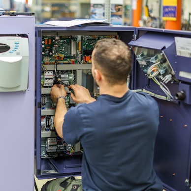 Ein junger Mann verdrahtet die Steuerung einer Großrundstrickmaschine.