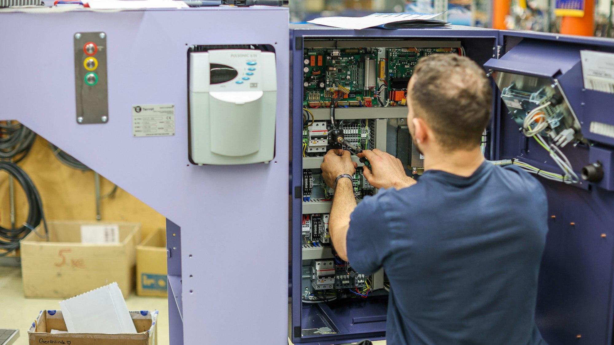 Ein junger Mann verdrahtet die Steuerung einer Großrundstrickmaschine.