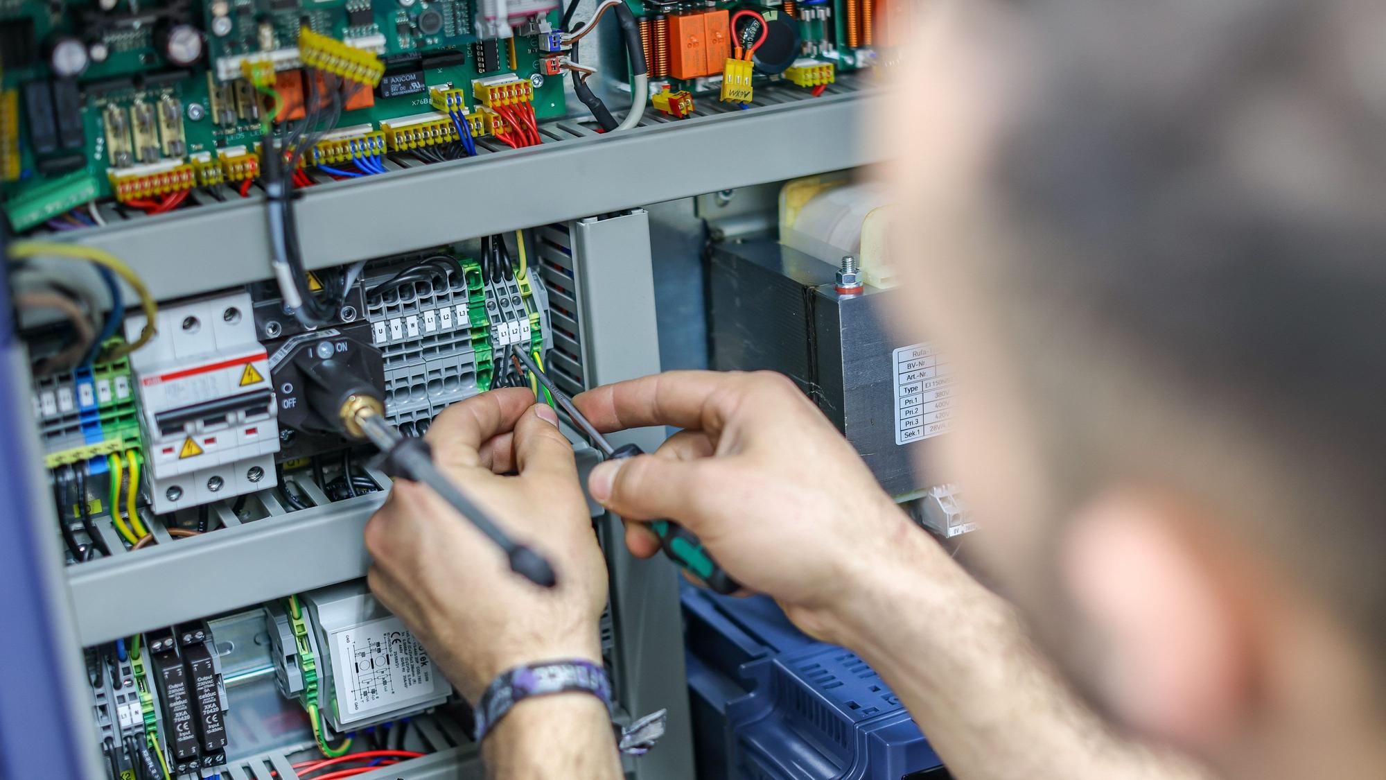 Ein Handwerker verdrahtet die Steuerung einer großen Maschine.
