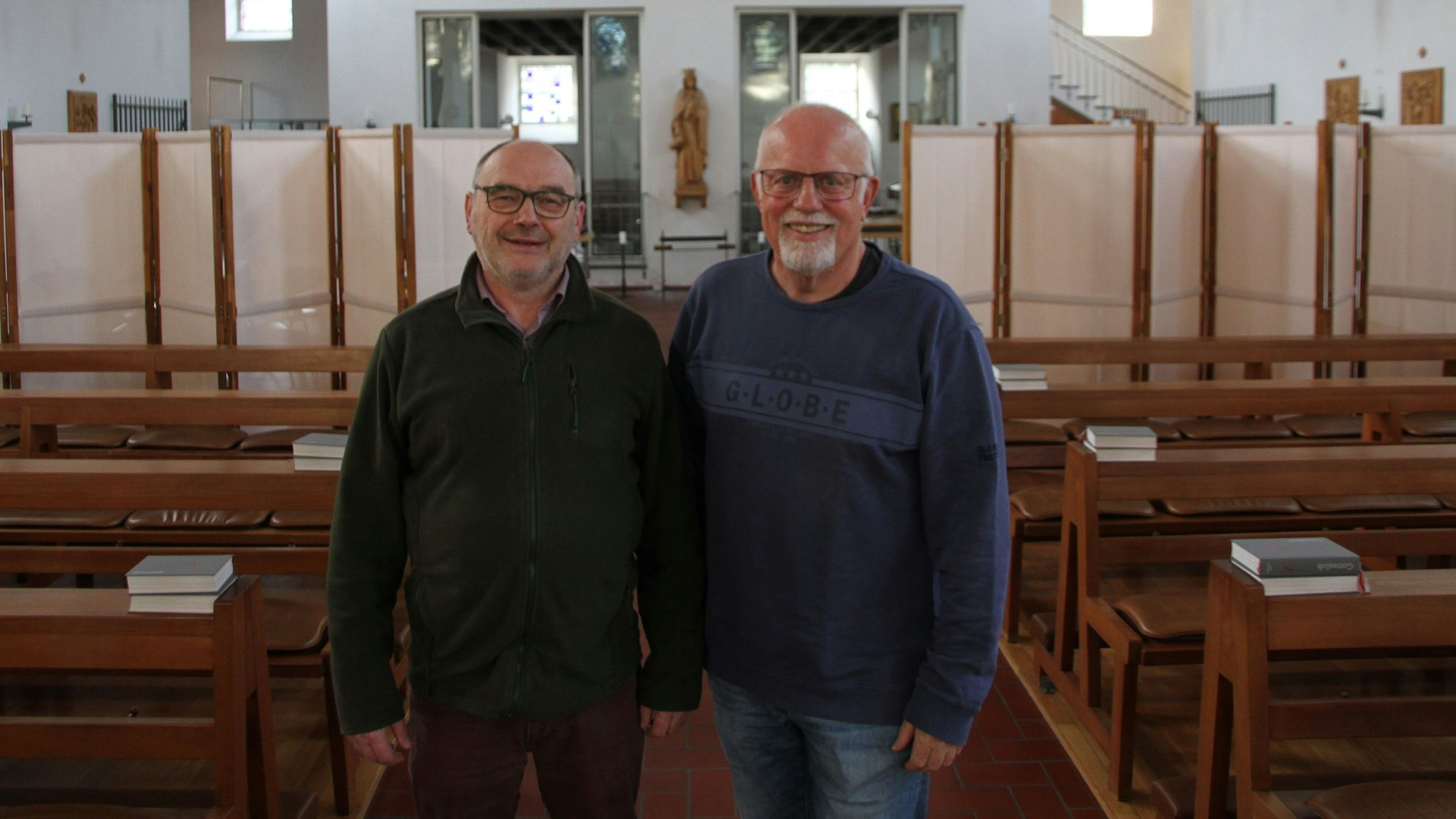 Zwei Männer im Mittelgang einer Kirche mit Kirchenbänken