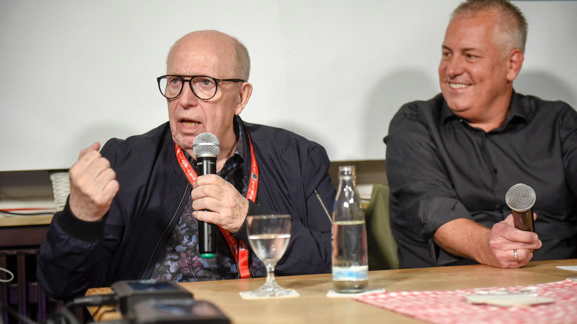 Zu sehen sind Reiner Calmund, der ein Mikrofon hält, und Marcel Schwamborn, der ebenfalls ein Mikrofon hält.