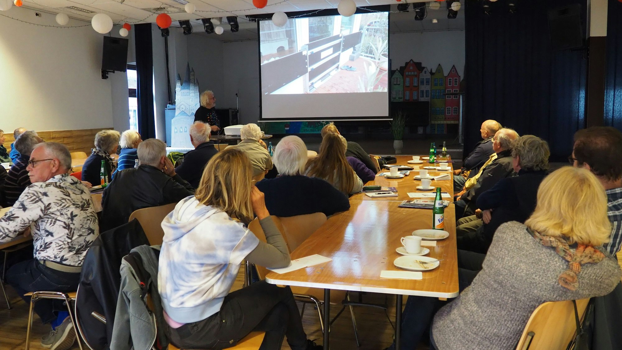 Ein Mann hält einen Vortrag, die Zuhörer schauen auf eine Leinwand.