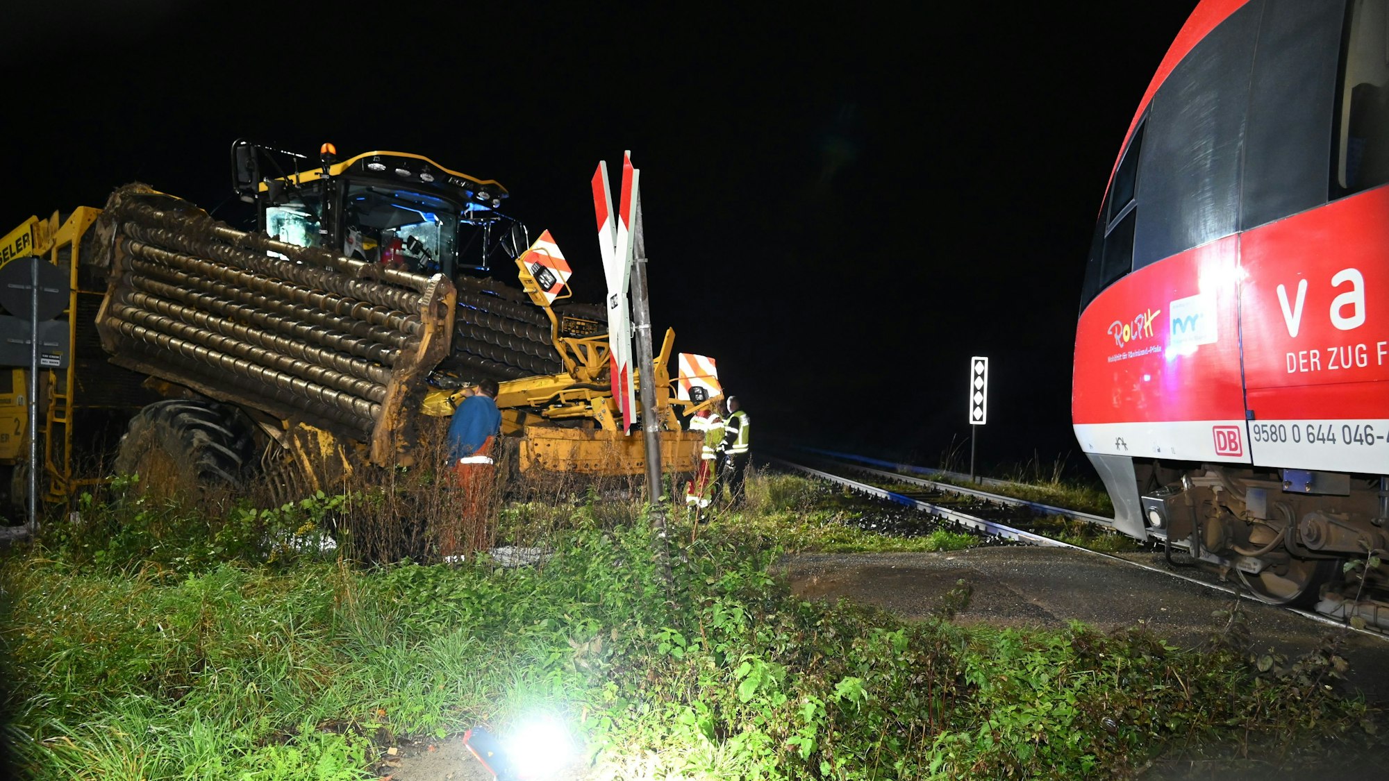 Ein Zug und eine Landmaschine stießen zusammen. Einsatzkräfte stehen um die Landmaschine herum, rechts ist der Zug zu sehen.