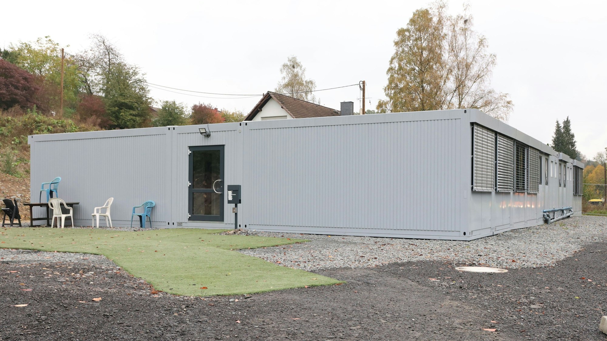 Vor einer Container-Unterkunft stehen leere Plastikstühle auf Kunstrasenteppichen.