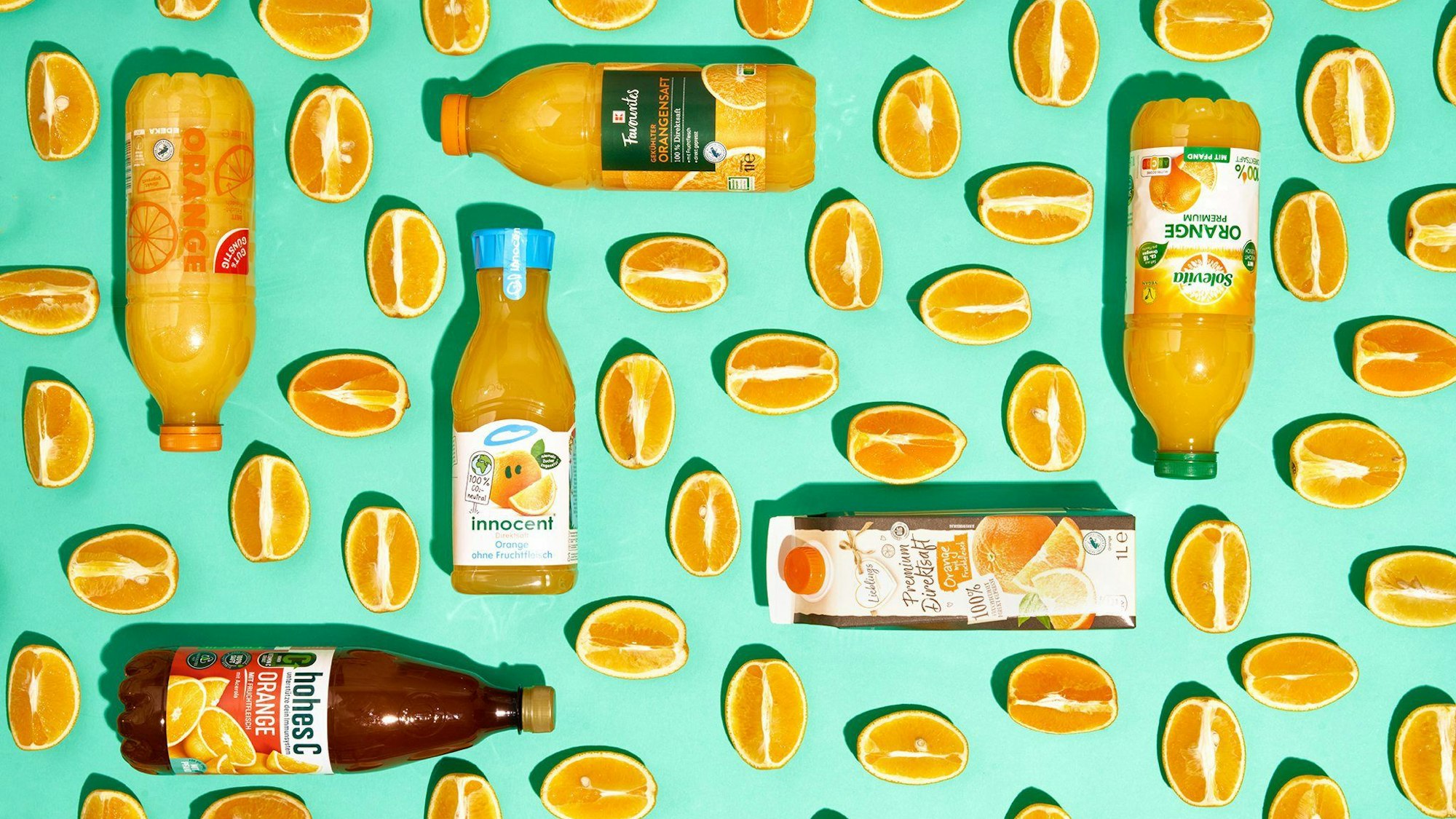 Sechs Flaschen mit Orangensaft zwischen Orangenspalten