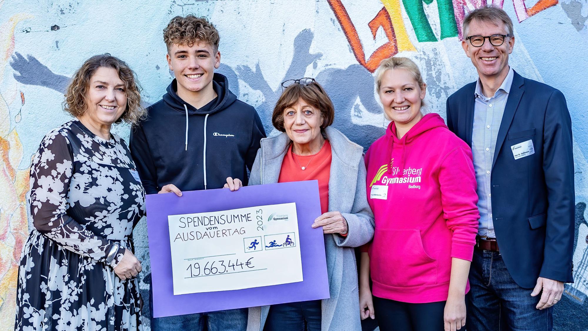Drei Frauen, ein Mann und ein Schüler zeigen einen übergroßen Scheck über knapp 20.000 Euro.
