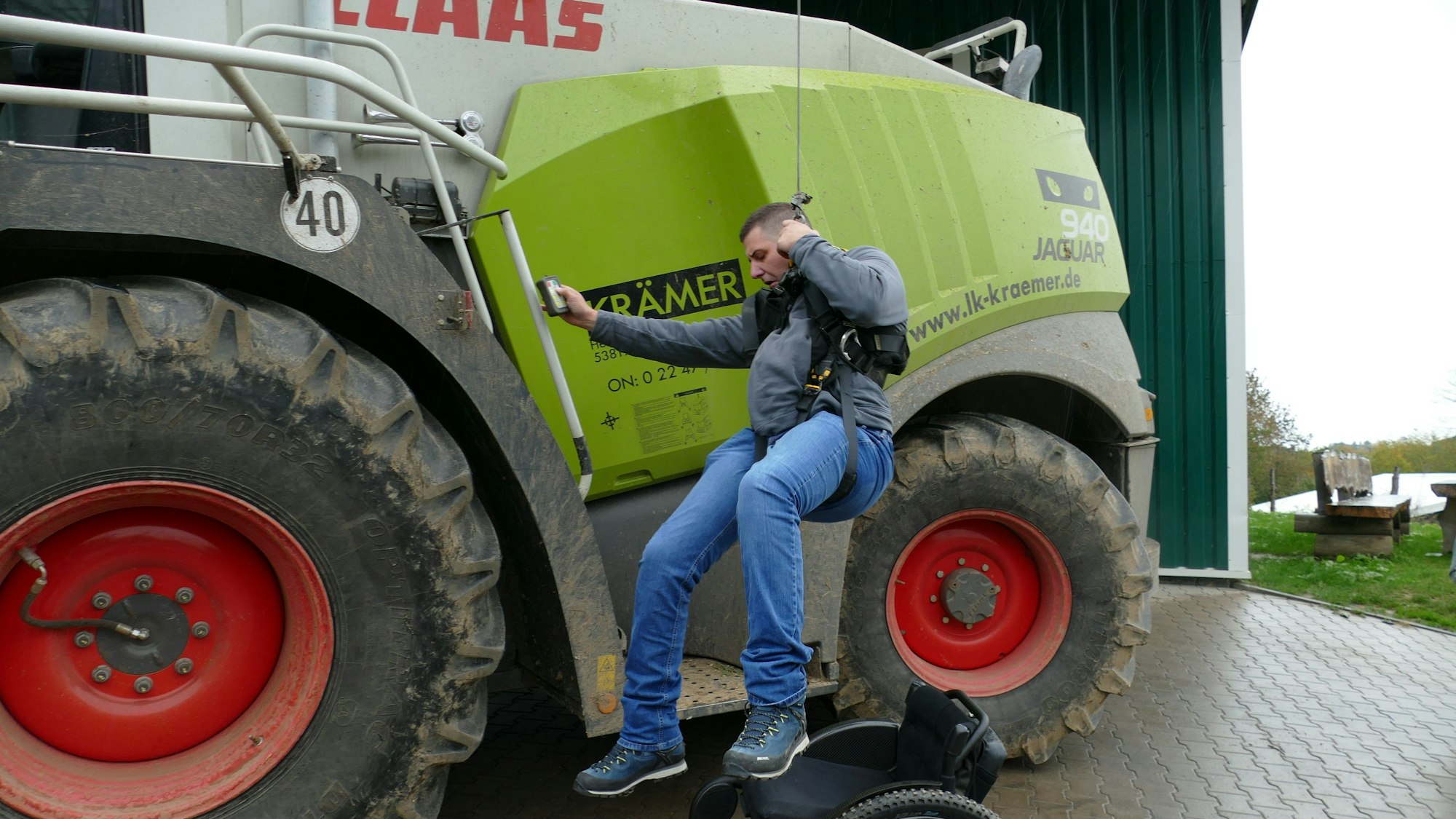 Ein Mann hängt an einem Kran vor einem Traktor.