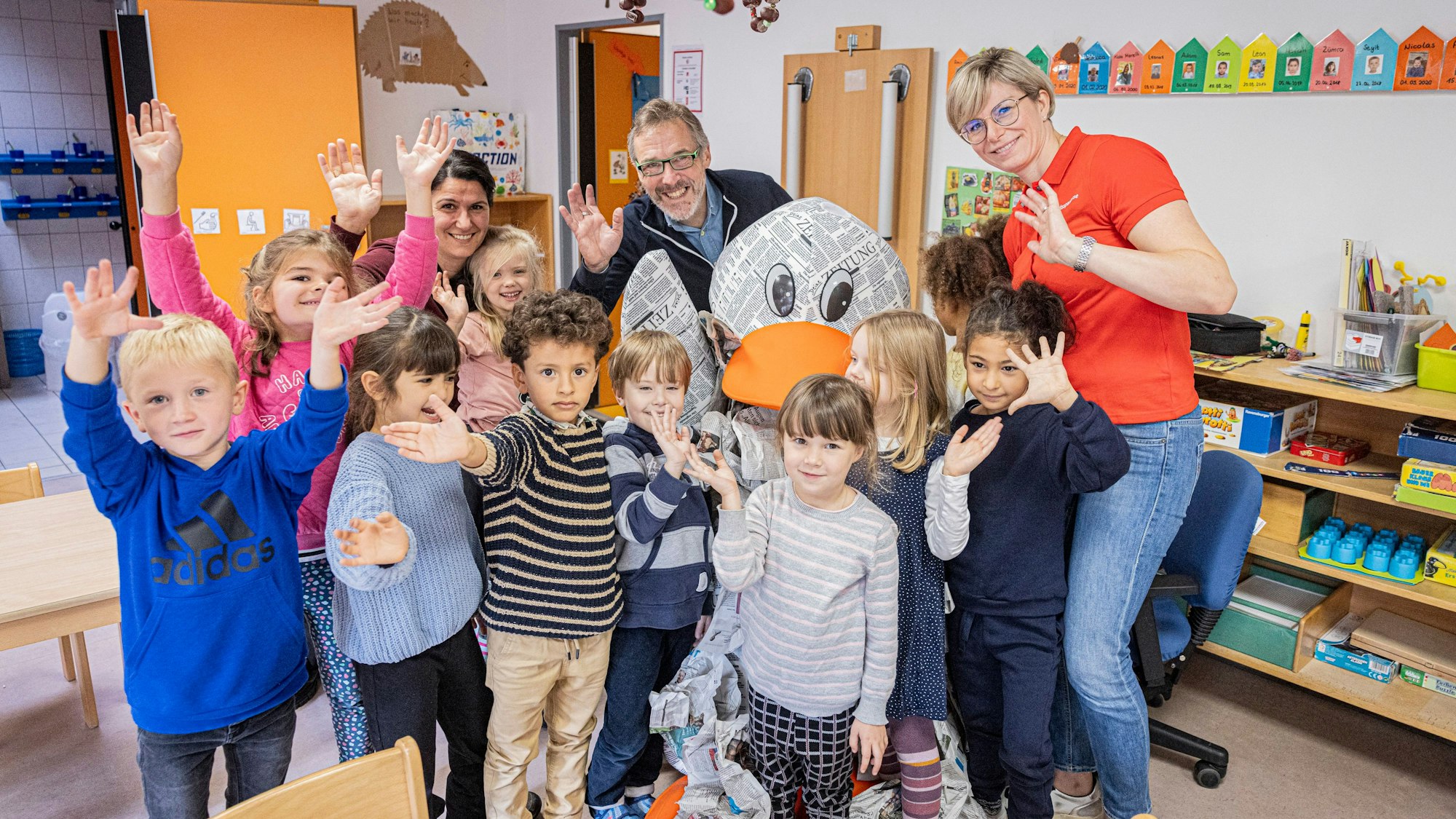 Die Kitakinder der „Pusteblume“ winken mit Rundschau-Redakteur Marcus Bierlein (mitte), Sonja Hertel von der Kreissparkasse Köln und Zeitungsente Paula Print in die Kamera.