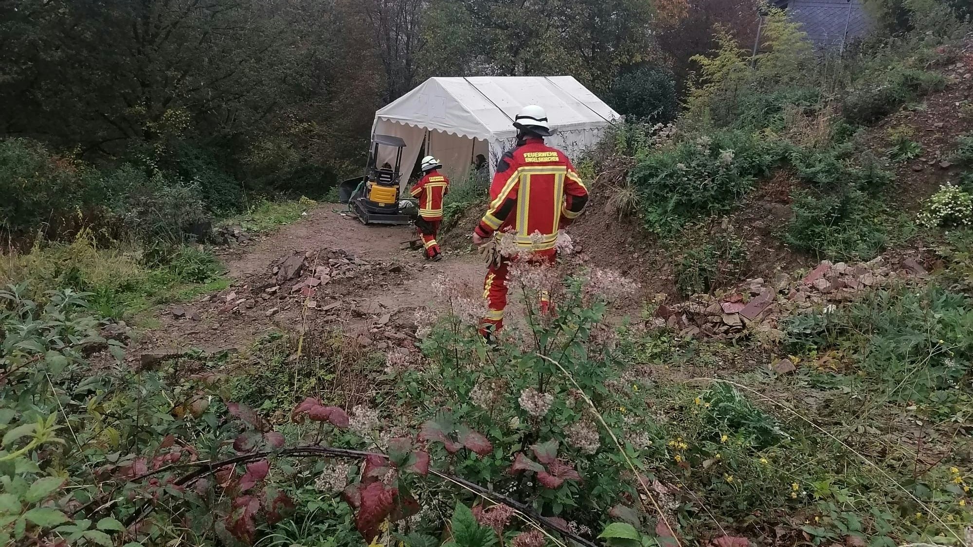 Feuerwehrleute am Hang mit dem Bagger.