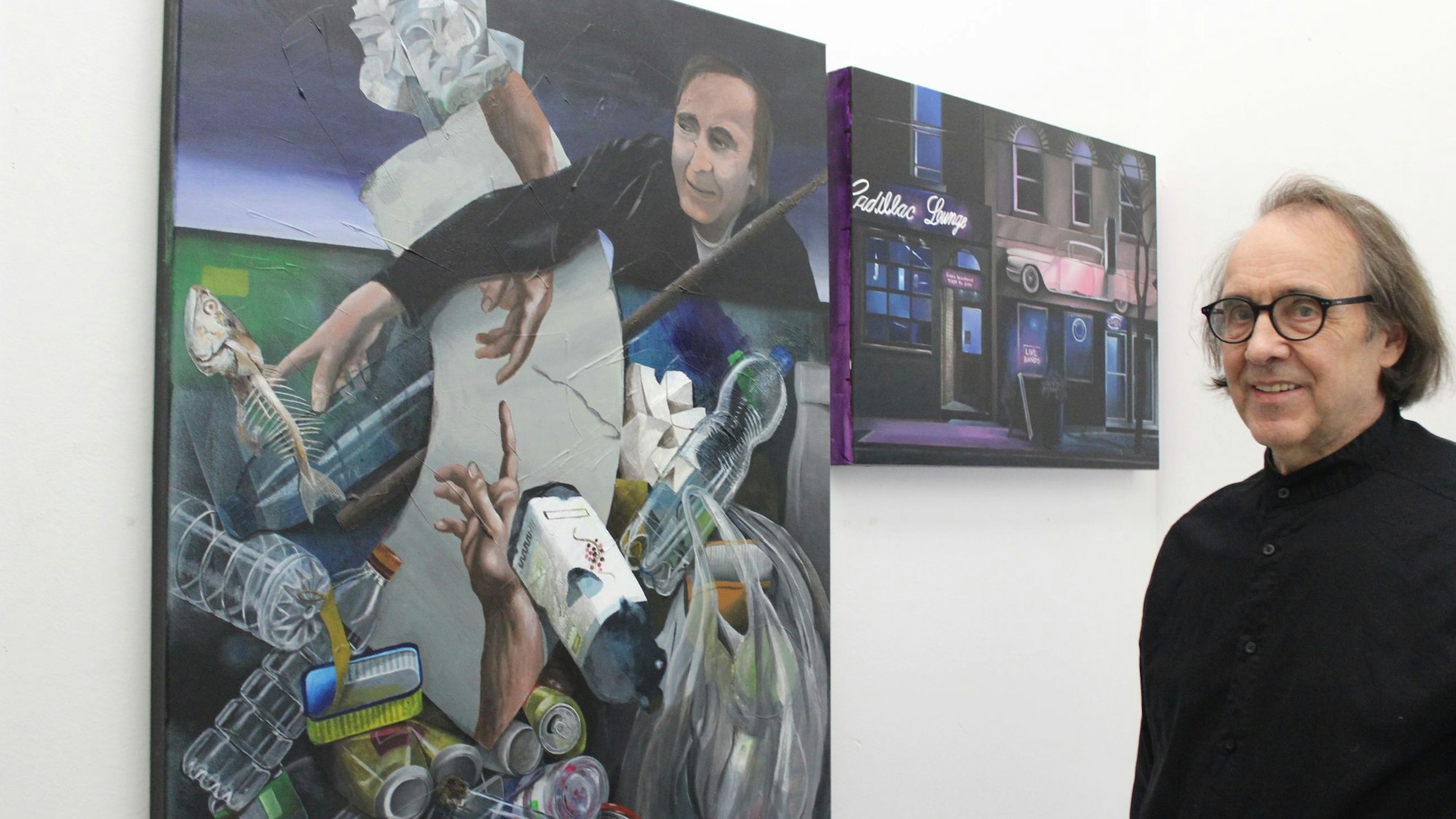 Auf dem Bild ist ein Künstler vor seinen Gemälden zu sehen.