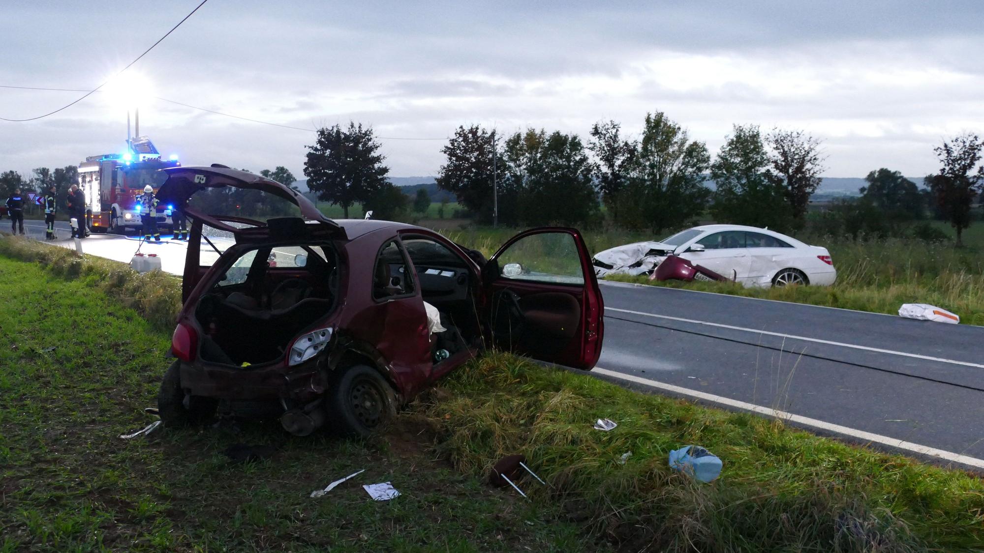 Zwei beschädigte Autos stehen neben einer Landstraße.