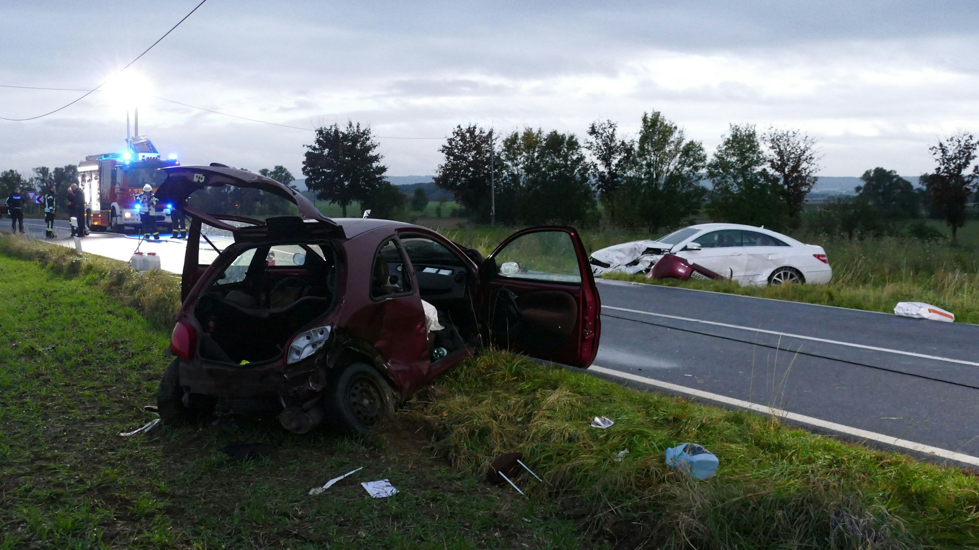 Zwei beschädigte Autos stehen neben einer Landstraße.