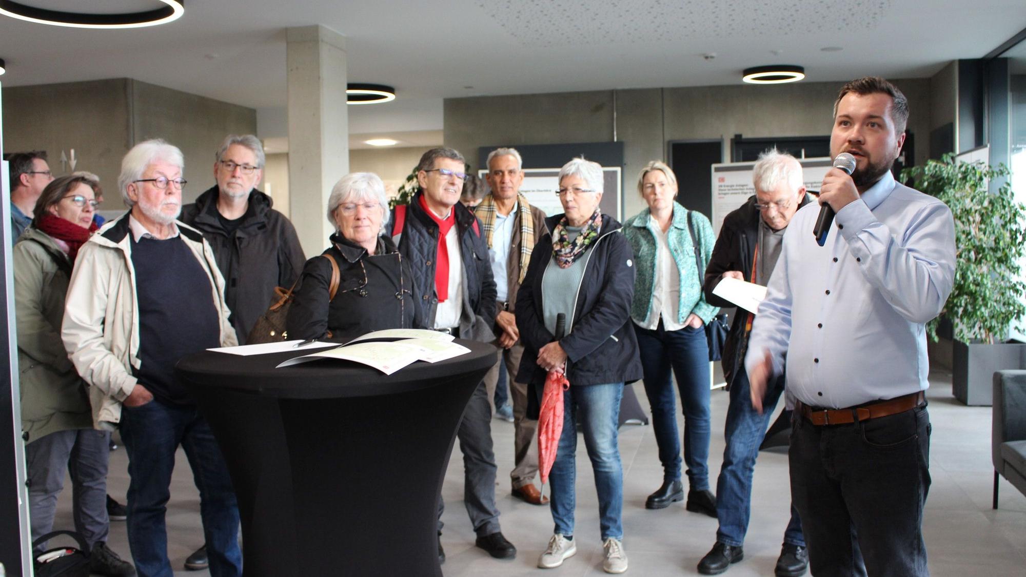 Projektleiter Nikolai Kopnow hält ein Mikrofon in der Hand, hinter ihm stehen einige der Besucher des DB-Bürgerdialogs.