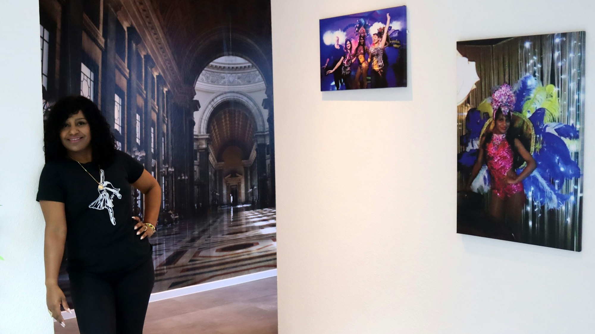 Yiset Durant Veranes lehnt lässig an die Wand im Eingangsbereich ihrer Tanzschule. An der Wand zeigen Bilder sie als Profitänzerin in Kuba. Im Hintergrund eine große Fotografie der Wandelhalle von Havanna.