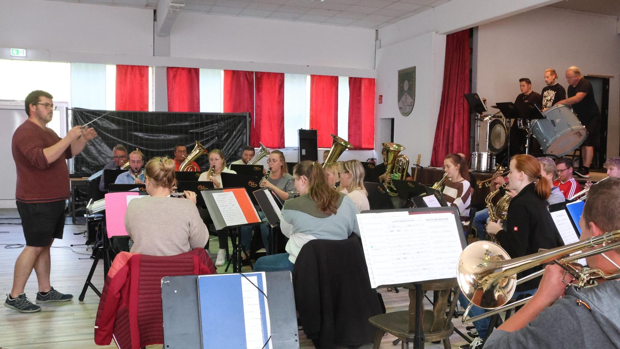 Ein Blasorchester und sein Dirigent proben in einem Saal.