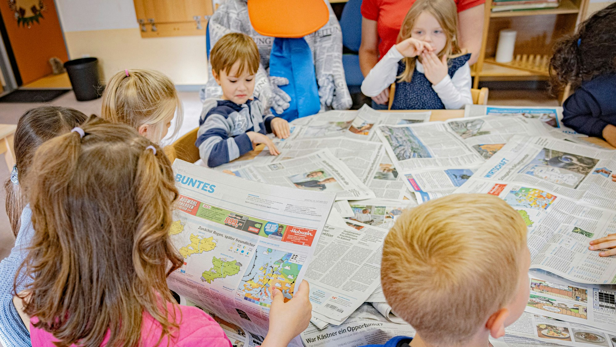 Kindergartenkinder sitzen an einem Tisch voller Rundschau-Zeitungen und stöbern durch die Ausgaben.