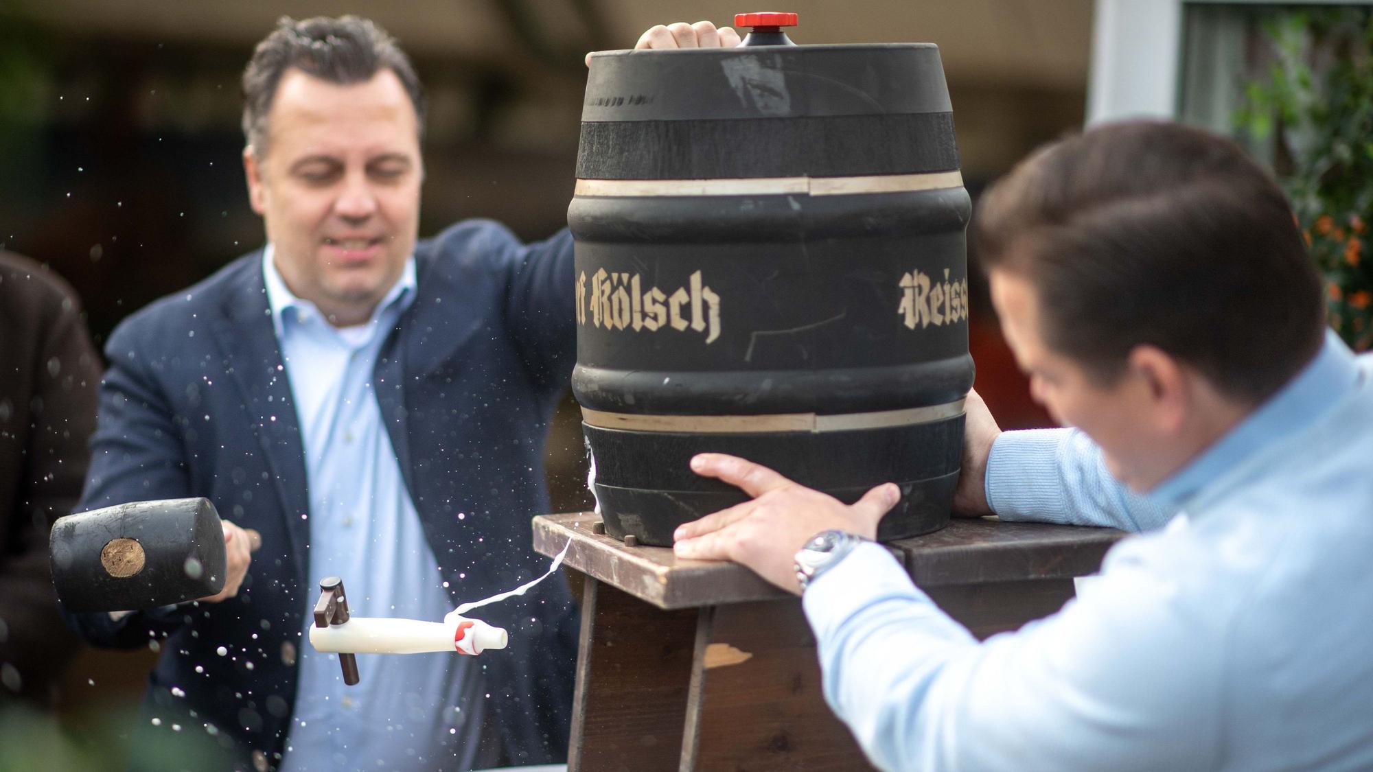 Das Bild zeigt den Bürgermeister, wie er sich beim Fassanstich versucht. Der Zapfhahn fliegt nach dem Schlag mit dem Hammer aber durch die Luft.