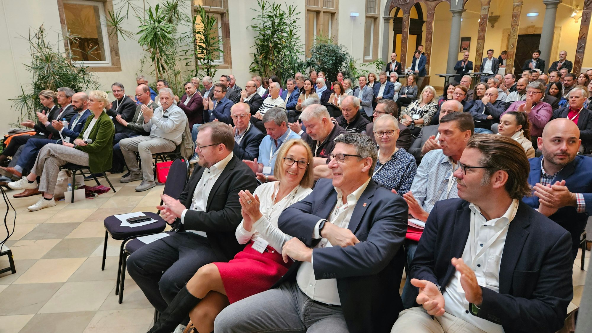 In einem Saal sitzen mehrere Dutzend Menschen und applaudieren.
