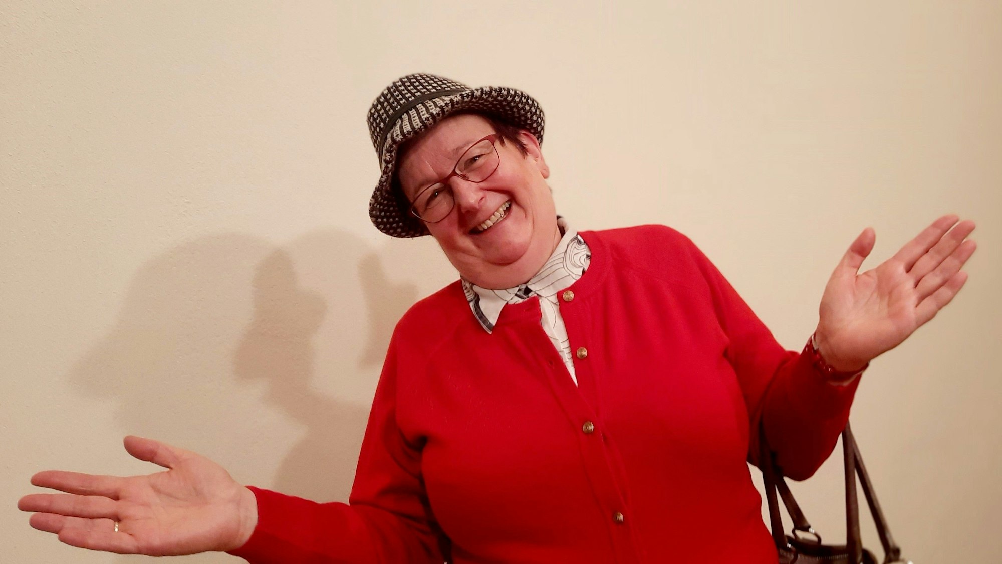 Ulrike Bömer posiert in einer roten Strickjacke mit ausgebreiteten Händen in ihrer Paraderolle als Erna Schabiewski.