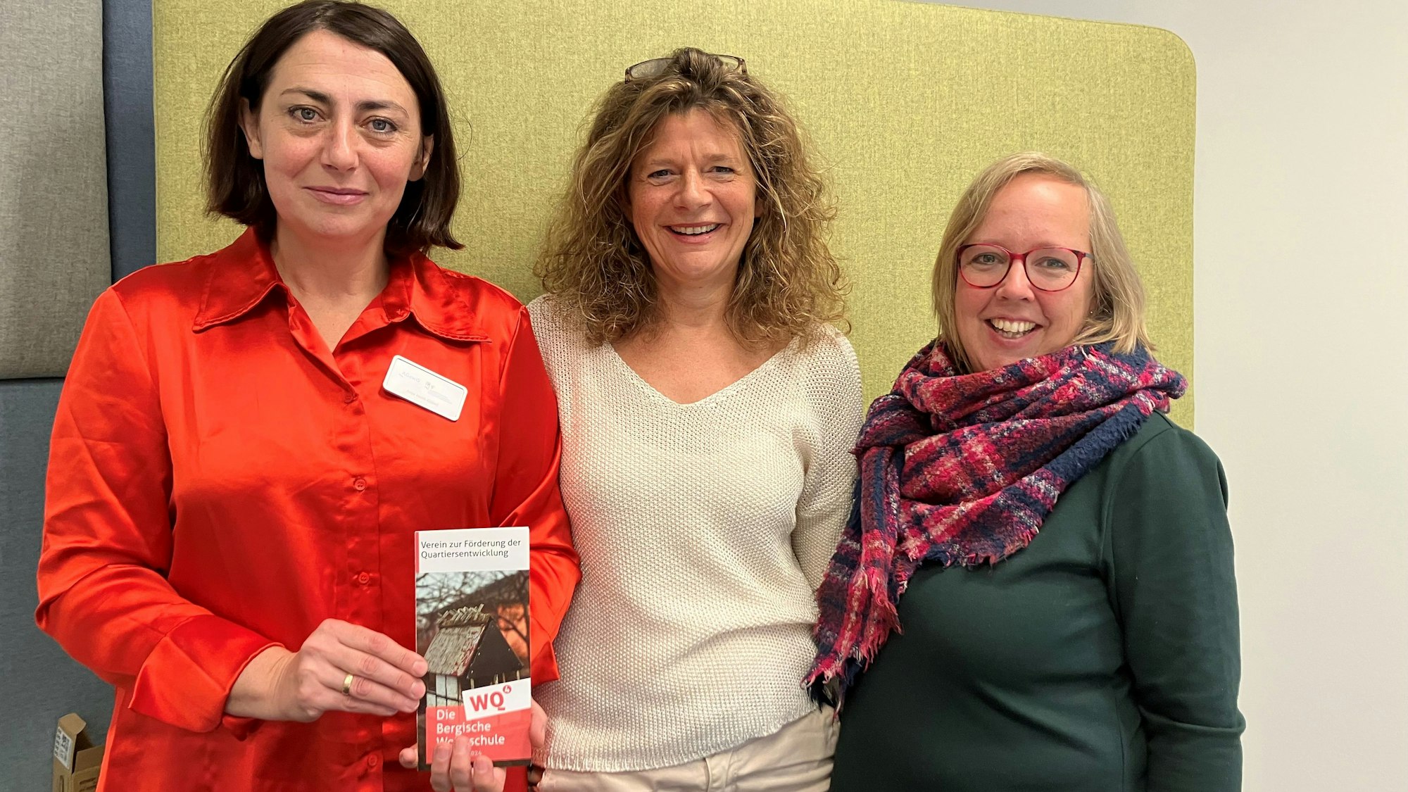 Drei Frauen stehen nebeneinander. Eine hält einen Flyer zur „Bergischen Wohnschule“ in den Händen.