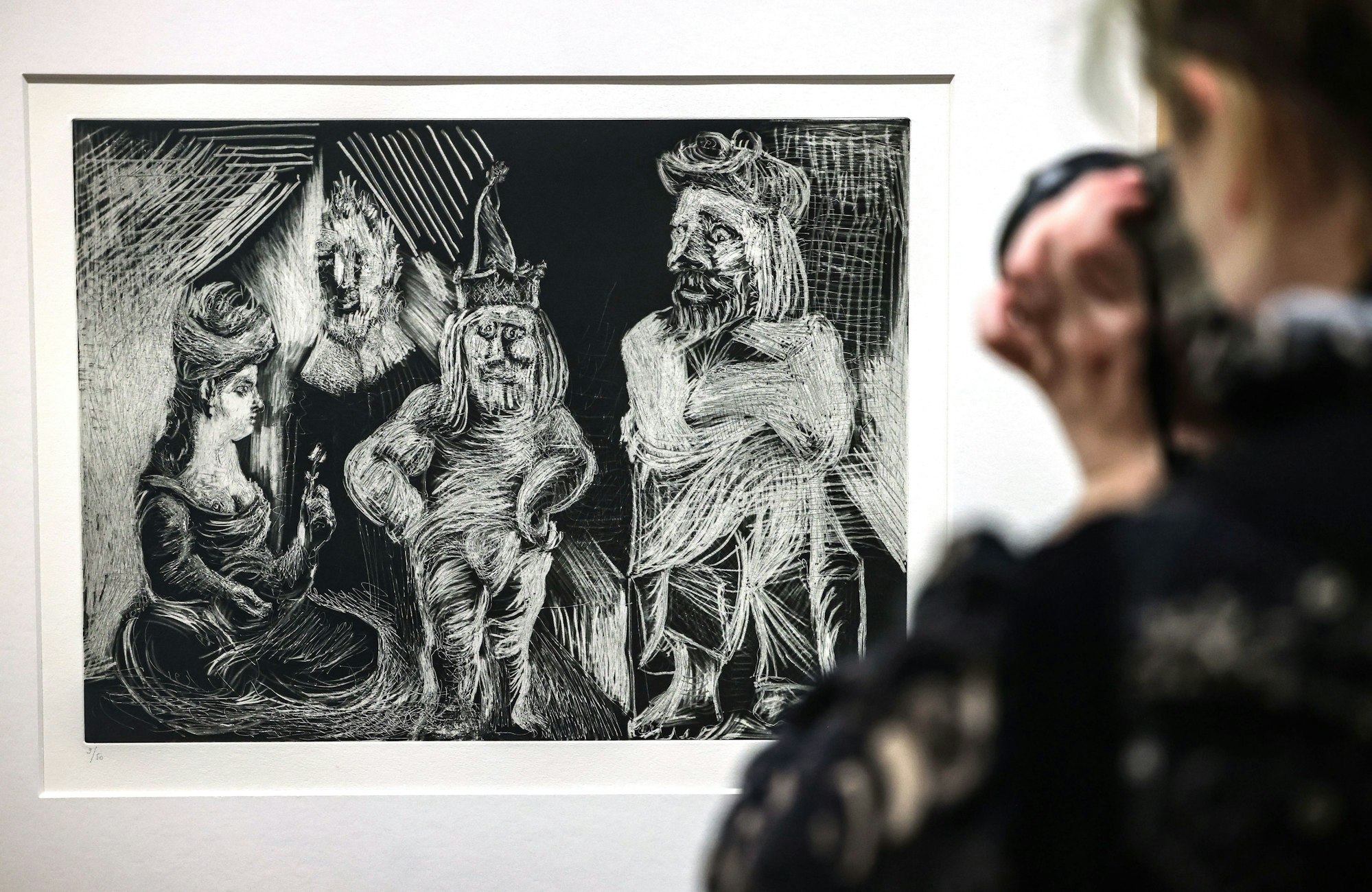 Eine Frau steht im Museum Ludwig vor der Radierung Frau mit Turban, alter Herr, Henker und Mann mit verrückten Augen von Pablo Picasso.