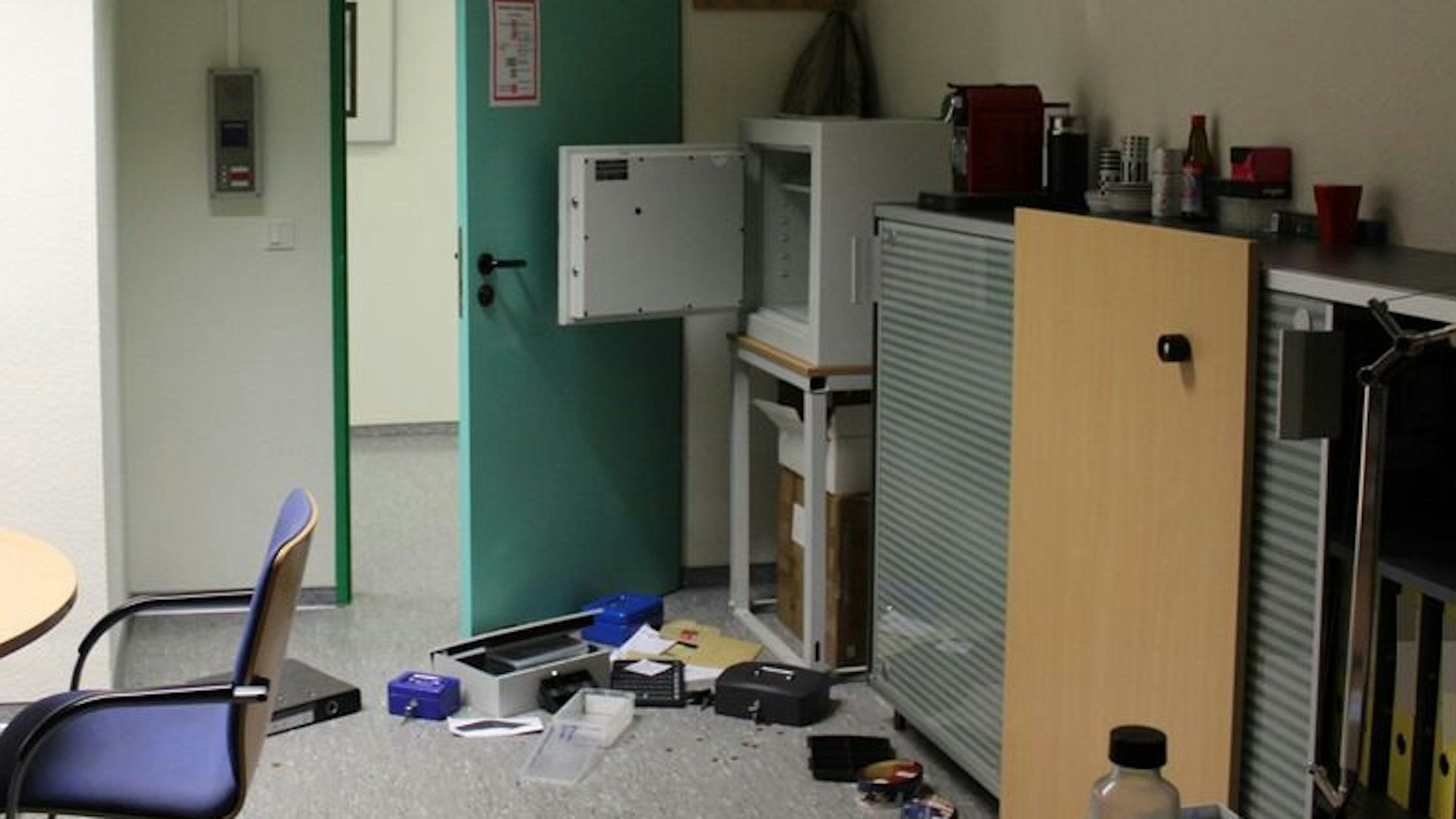 Ein Raum ist durchwühlt, eine Tresortür steht offen, auf dem Boden liegen Gegenstände verteilt.