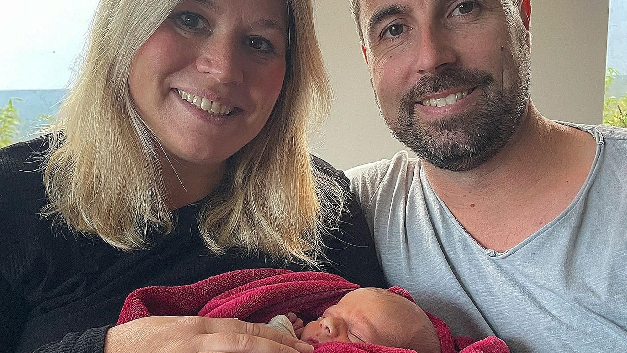 Jennifer und Krishan Meuren halten ihren neugeborenen Sohn Levi in einer roten Decke im Arm.