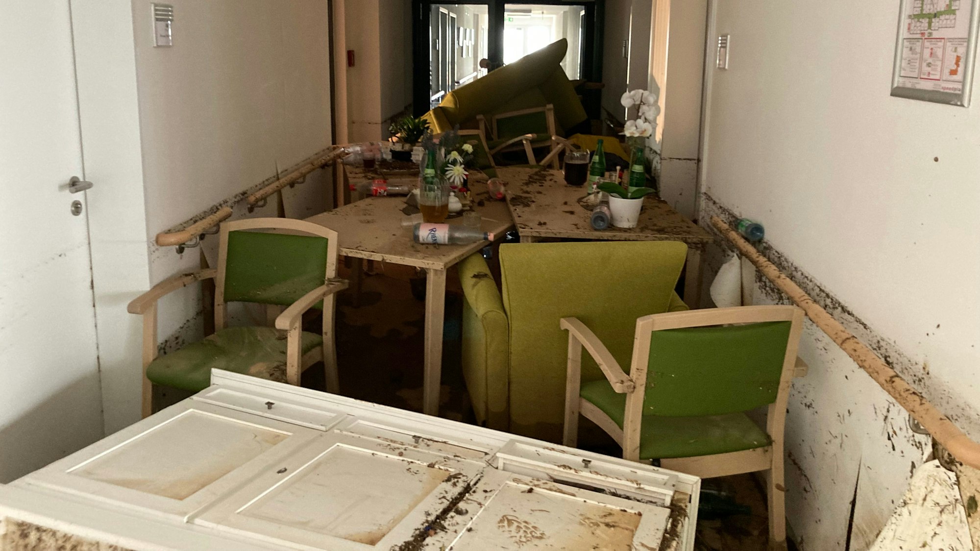 In einem schlammigen Flur sind beschädigte Möbel gestapelt.