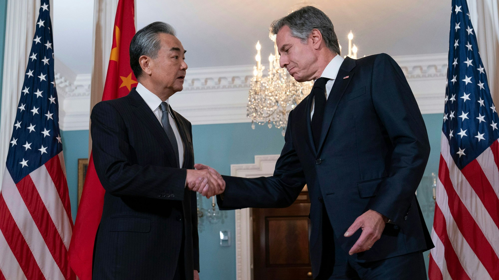 Zwei Männer in Anzügen schütteln sich die Hand. Im Hintergrund befinden sich amerikanische Flaggen sowie eine chinesische Flagge.