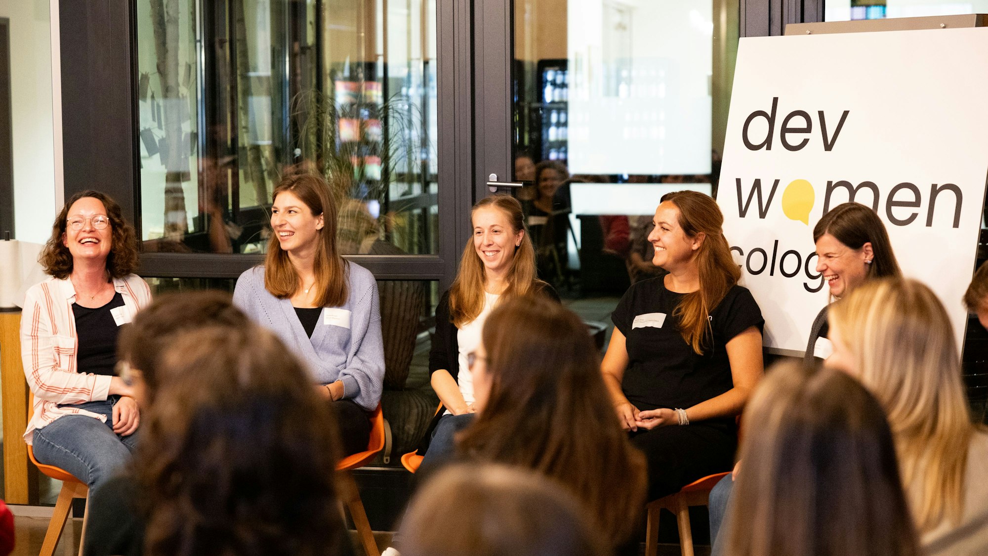 Fünf junge Frauen sitzen auf Stühlen nebeneinander und diskutieren vor Publikum.