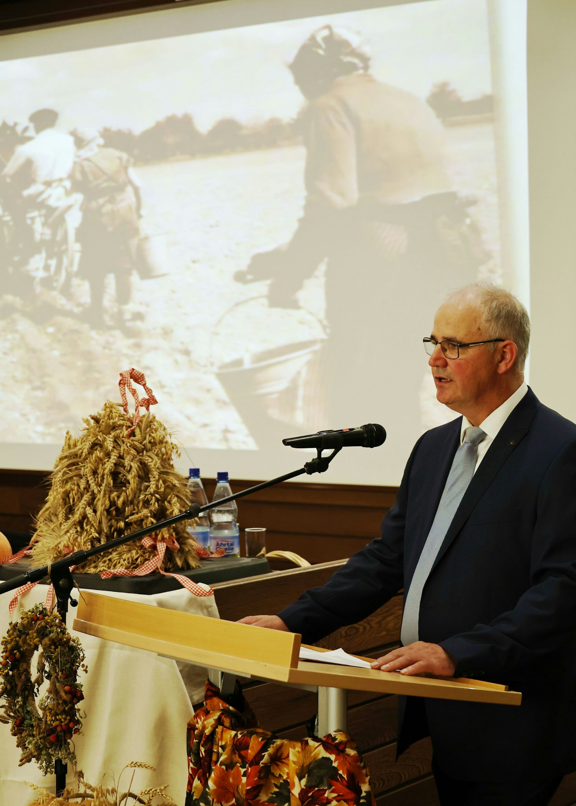 Helmut Dahmen bei seiner Rede, im Hintergrund die Projektion von Bäuerinnen auf einem Feld.