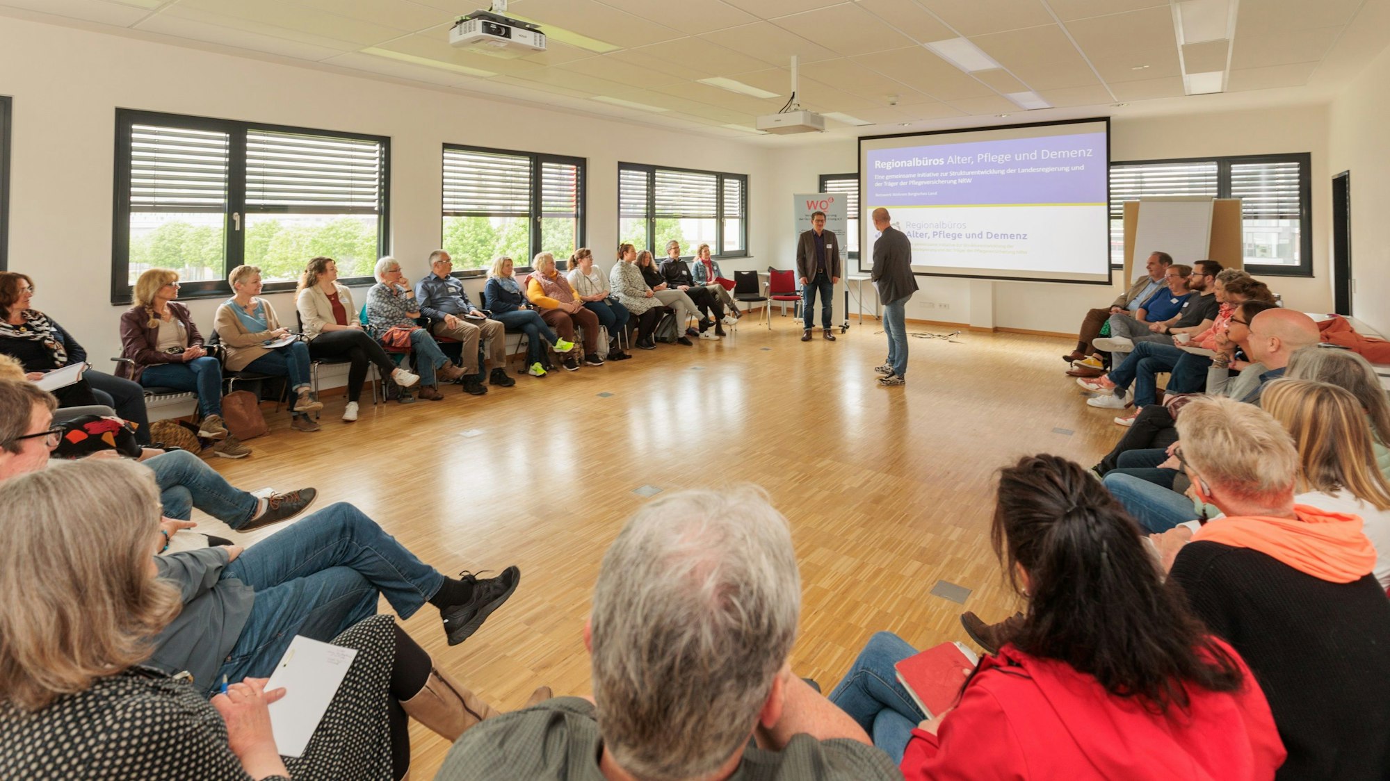 Mehrere Menschen sitzen bei einem Vortrag in einem großen Kreis.