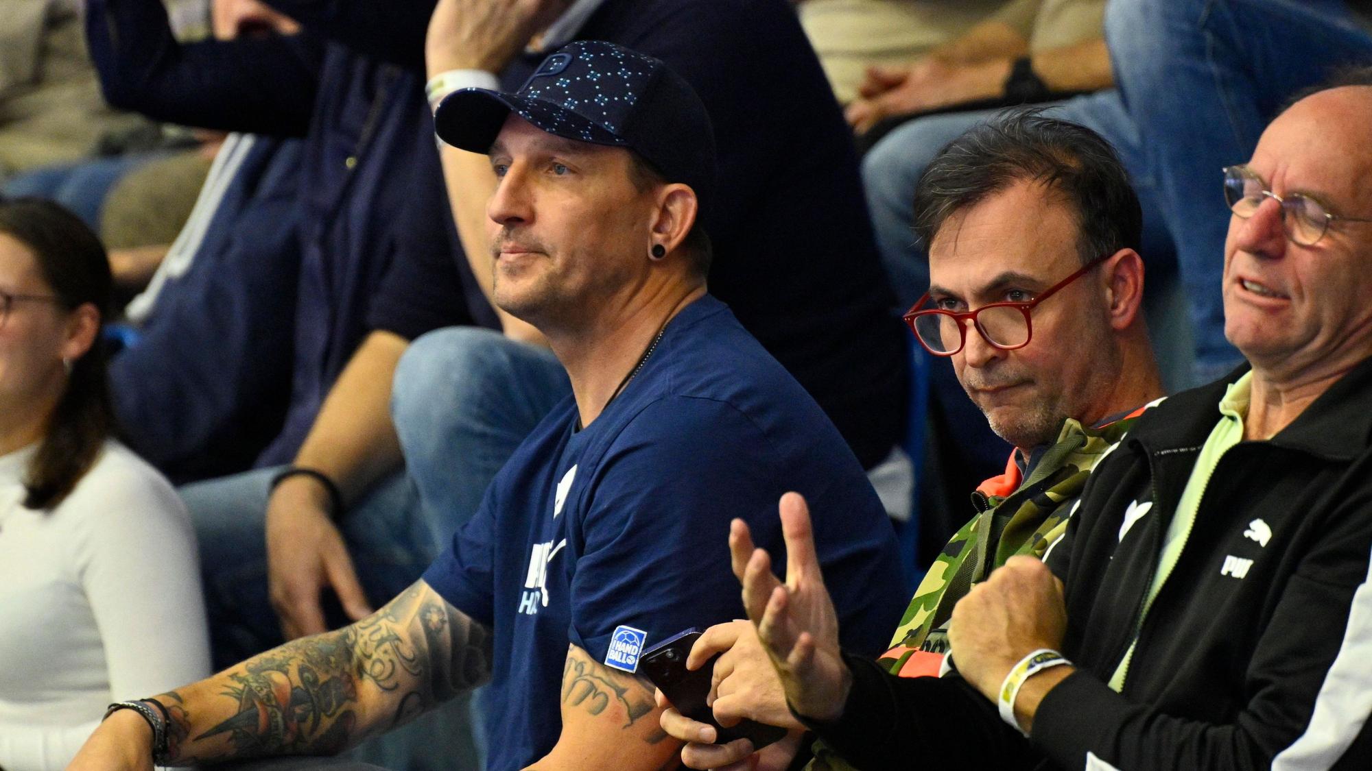 Mehrere Männer sitzen im Publikum bei einem Handballspiel.