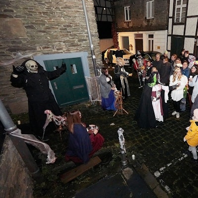 Eine Geisterfigur mit Totenkopf und dunklem Umhang erschreckt Besucher auf der Straße.