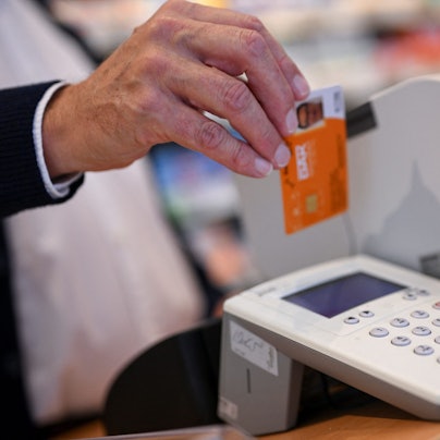 Eine Person legt die Gesundheitskarte eines Patienten in ein Kartenlesegerät in einer Apotheke.