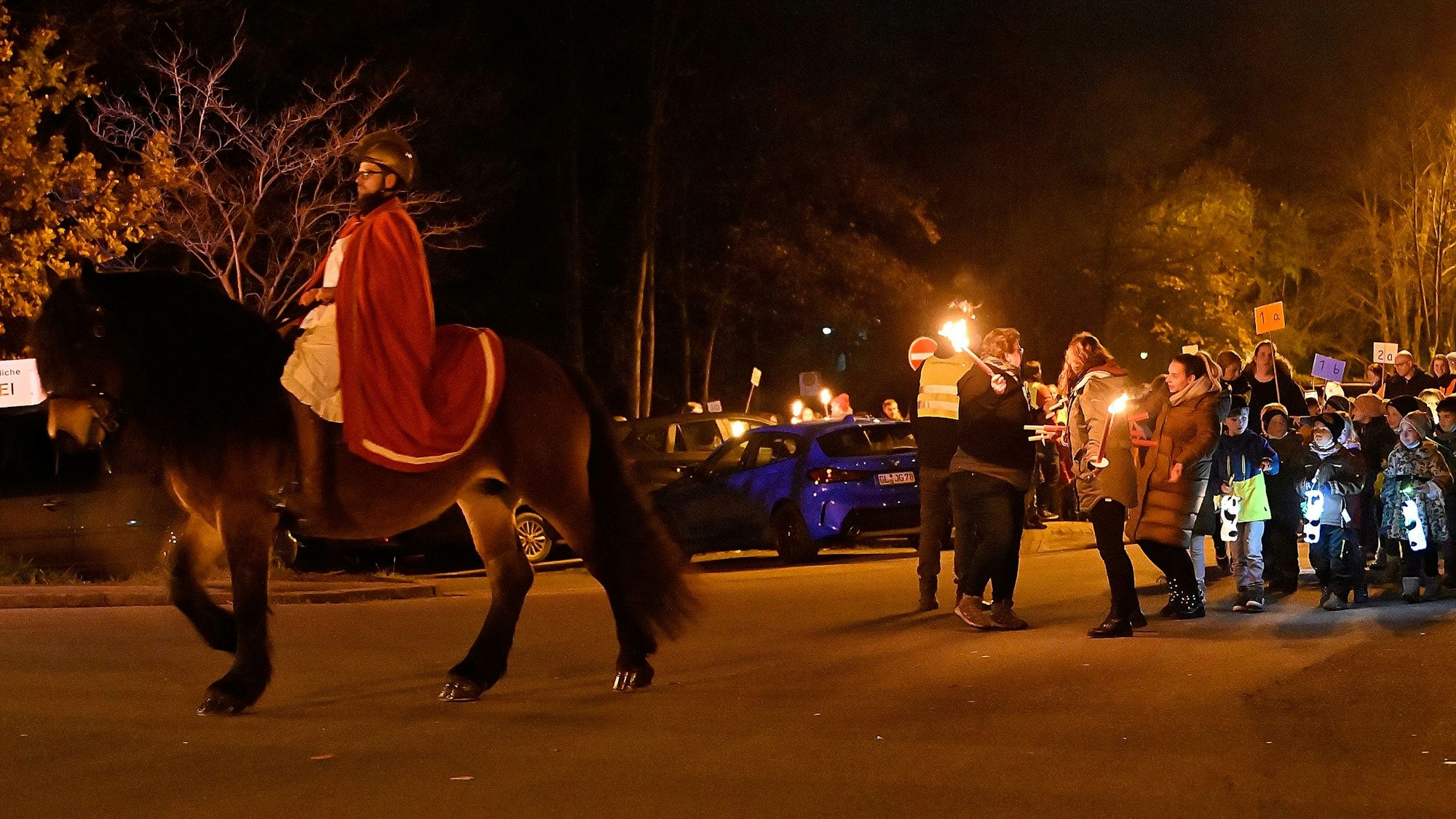 Ein als Sankt Martin verkleideter Mann reitet auf einem Pferd, dahinter gehen Kinder mit leuchtenden Laternen.