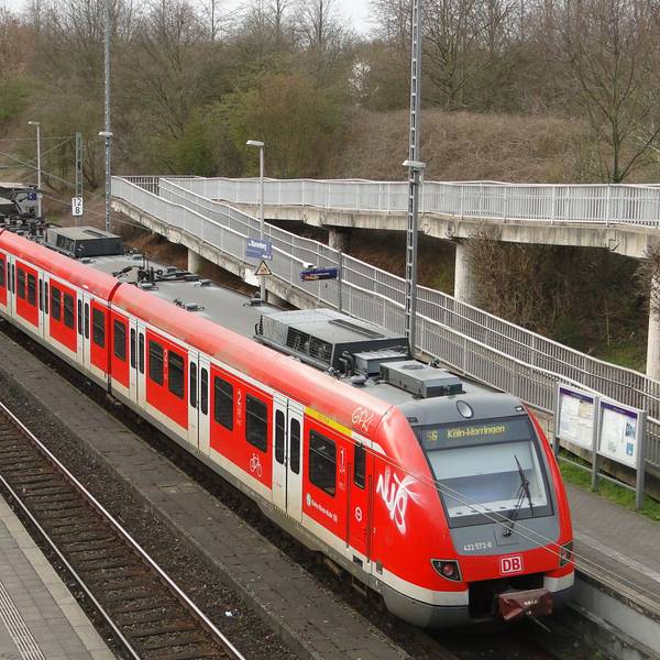 Eine S-Bahn steht an einer Haltestelle, die durch eine Fußgängerbrücke erreichbar ist.