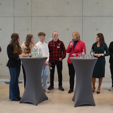 Bundestagspräsidentin Bärbel Bas mit Schülern an Stehpulten.