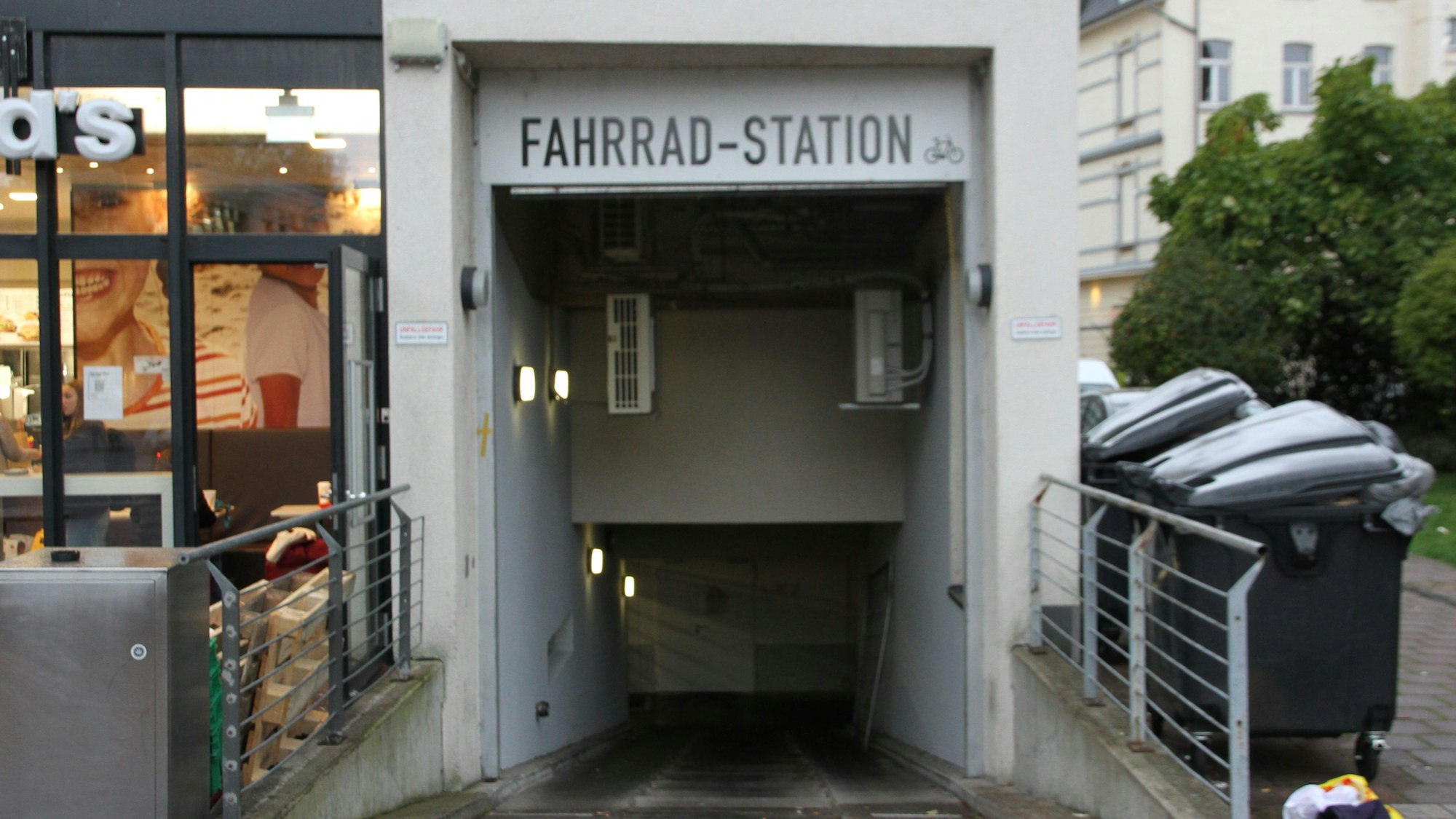 Eingang zu einer Fahrrad-Tiefgarage zwischen einem Schnellimbiss und Müllcontainern