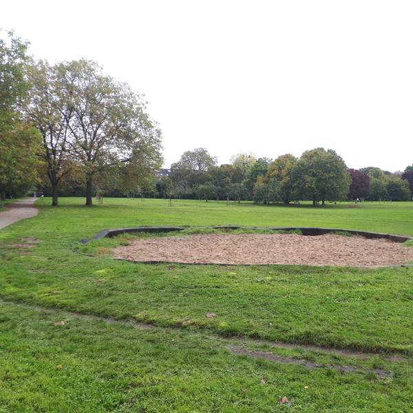 Eine ovale Sandfläche in einer Rasenfläche in einem Park ist zu sehen.