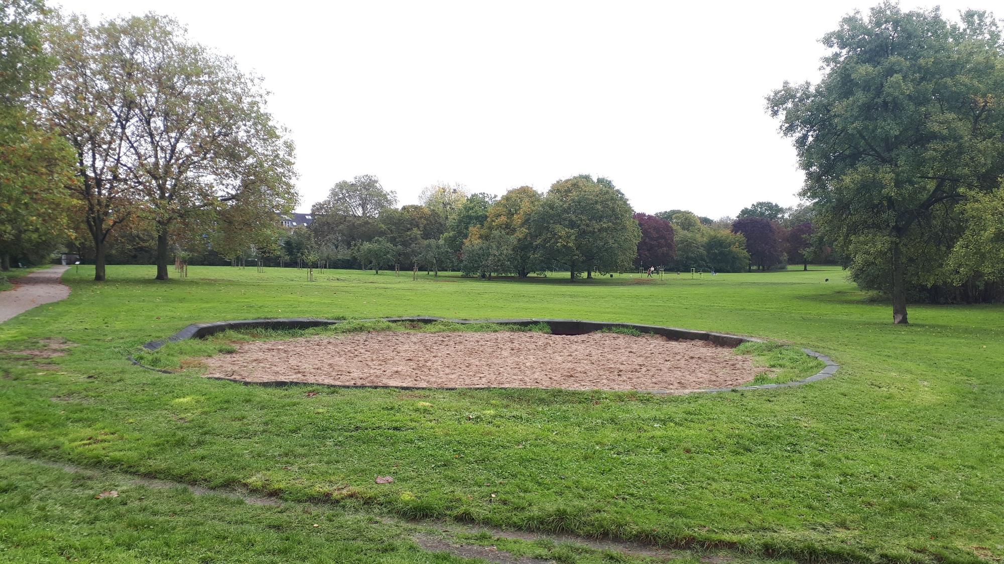 Eine ovale Sandfläche in einer Rasenfläche in einem Park ist zu sehen.