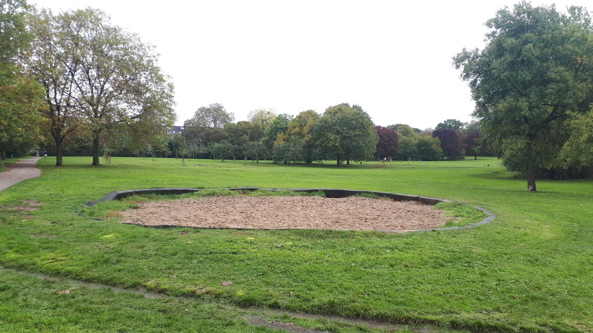 Eine ovale Sandfläche in einer Rasenfläche in einem Park ist zu sehen.
