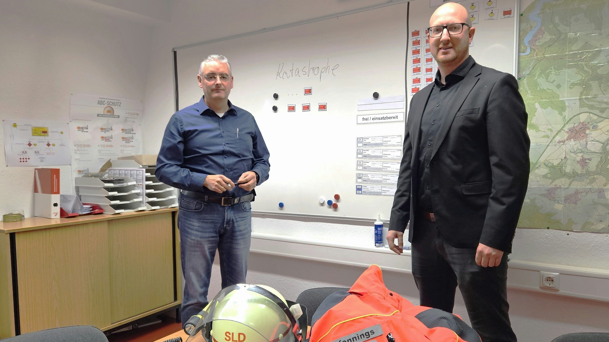Wolfgang Fuchs (l.), Leiter der Stabsstelle für den Katastrophenschutz, und Bürgermeister Ingo Pfennings stehen vor einer Schreibtafel mit dem Wort Katastrophe.