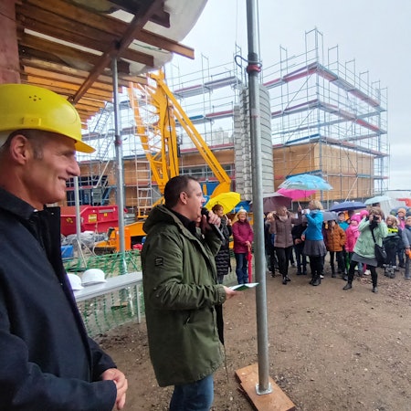 Zwei Männer und viele Kinder mit Regenschirmen auf einer Baustelle