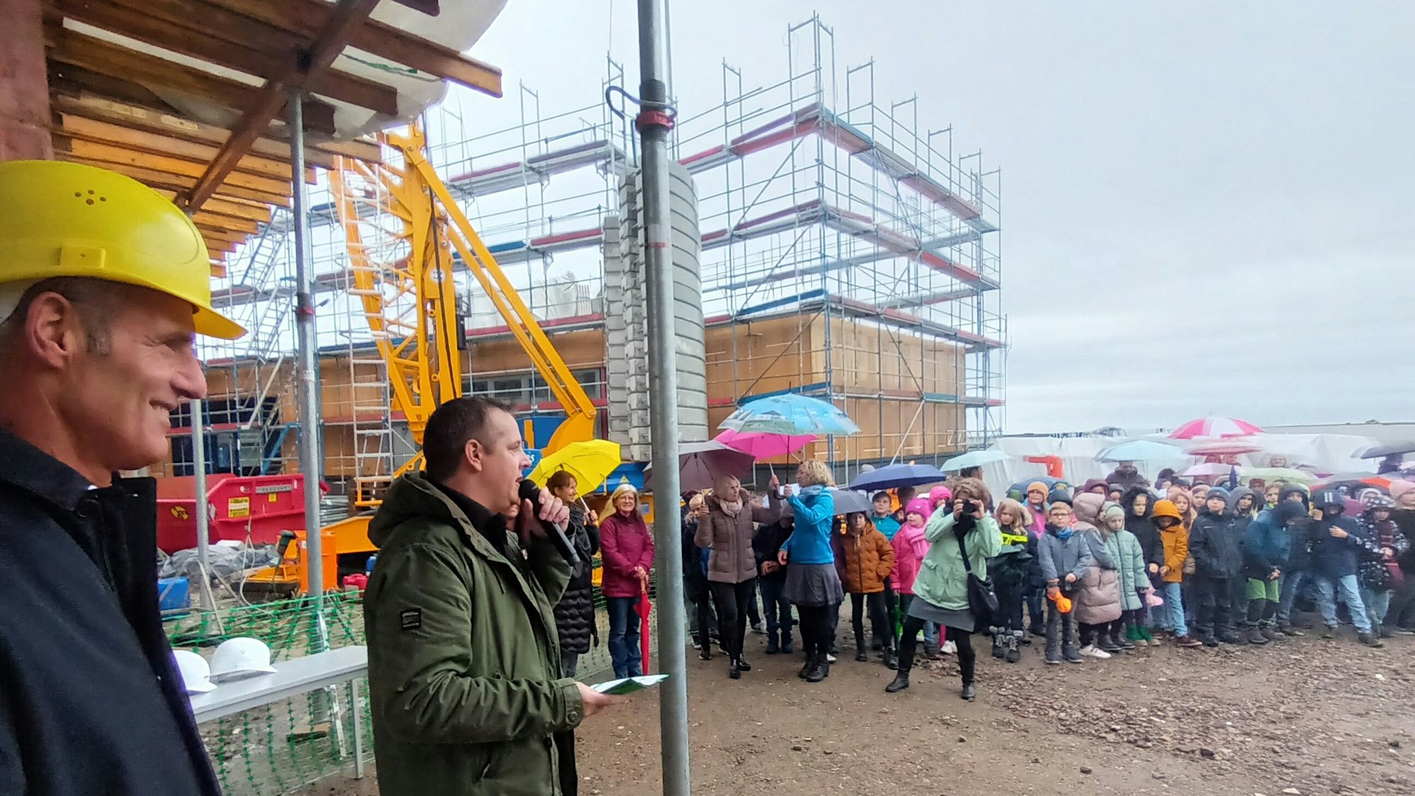 Zwei Männer und viele Kinder mit Regenschirmen auf einer Baustelle