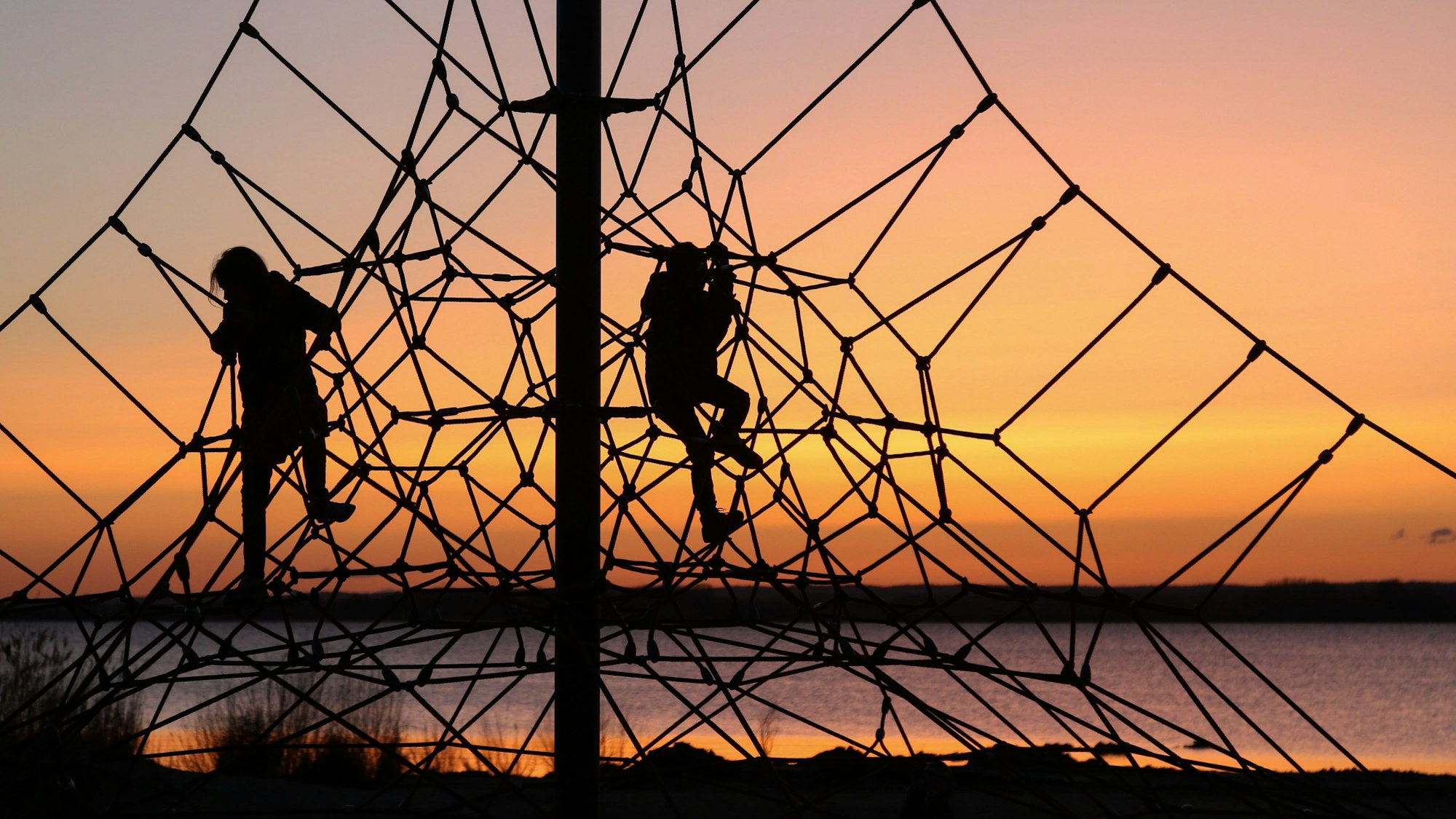 Kinder klettern vor der untergehenden Sonne auf einem Klettergerüst am Strand.